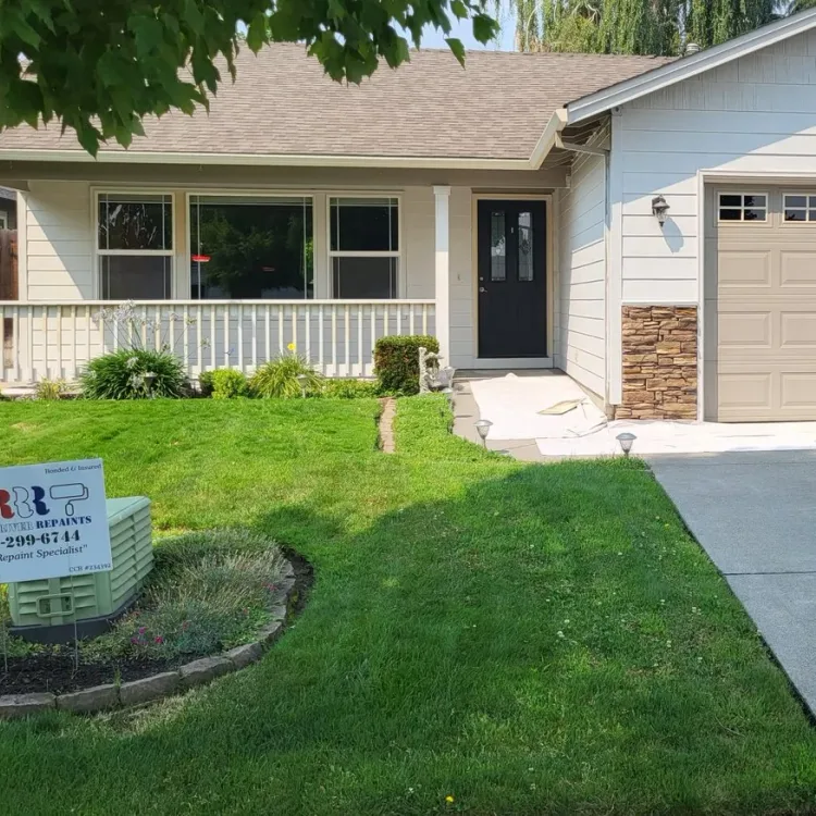 A cream house with a white porch rail and a Rogue River Repaints yard sign on the lawn