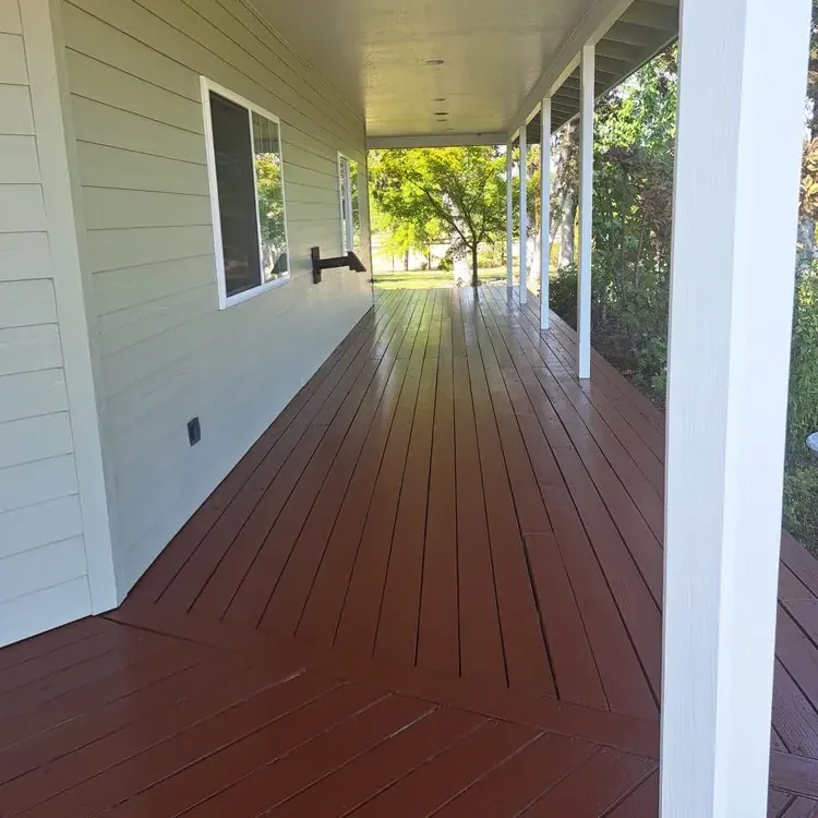 A covered porch floor freshly stained red-brown alongside white-painted siding