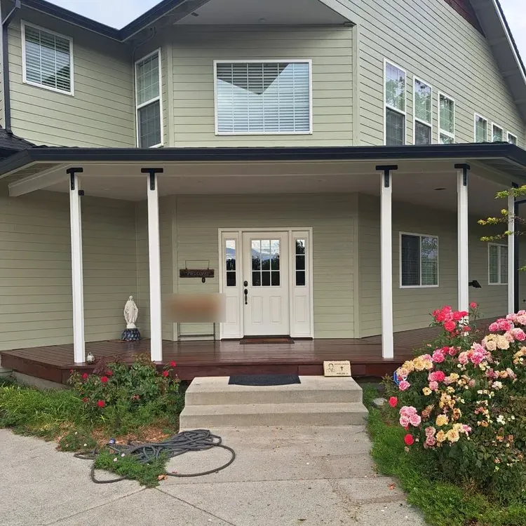 A two-story house repainted sage green with white porch columns and a stained porch deck