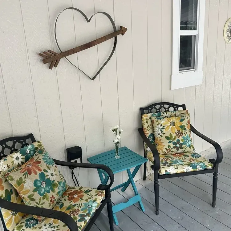 A covered porch with freshly painted siding and white window trim, two patio chairs and a small table