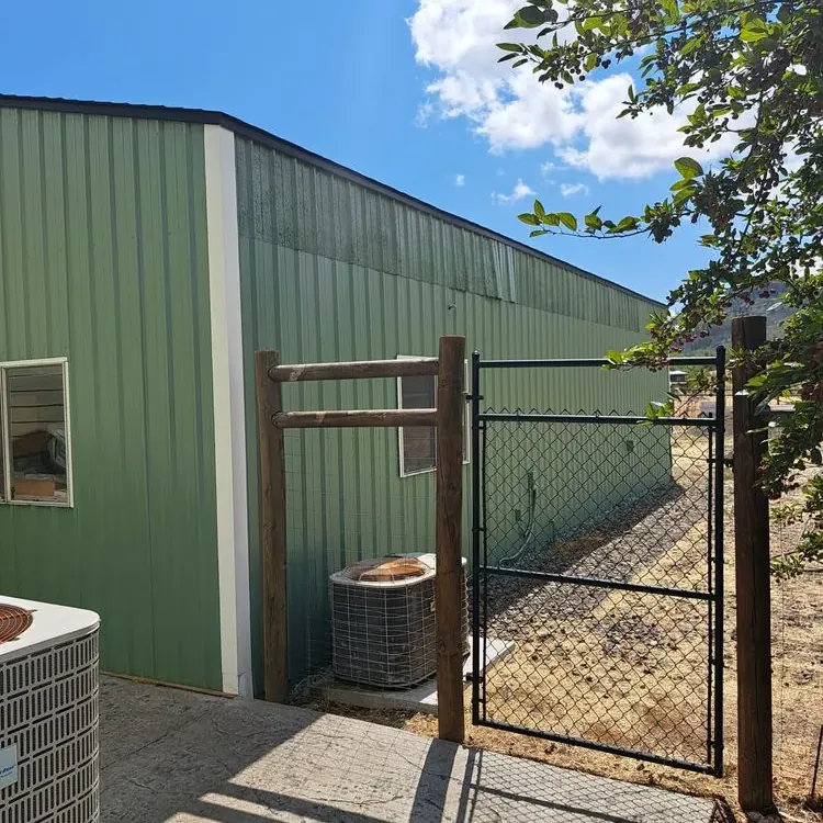 A green metal outbuilding with white trim beside a chain-link gate, freshly painted
