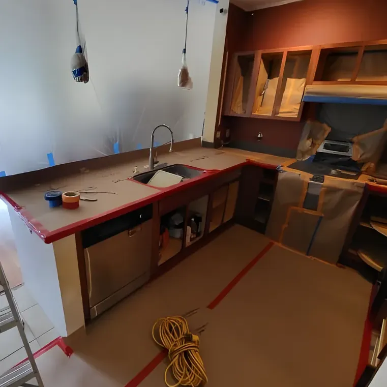 A kitchen masked off with tape and plastic, its counters and floor covered for painting
