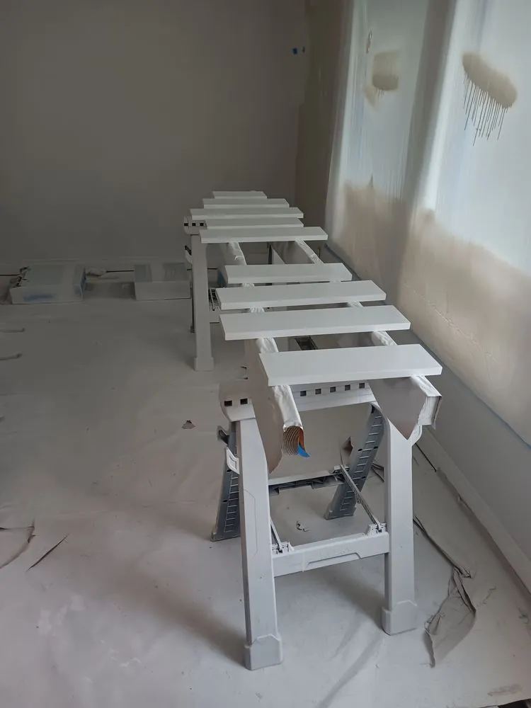 Drawer fronts drying on sawhorses in a room covered in plastic