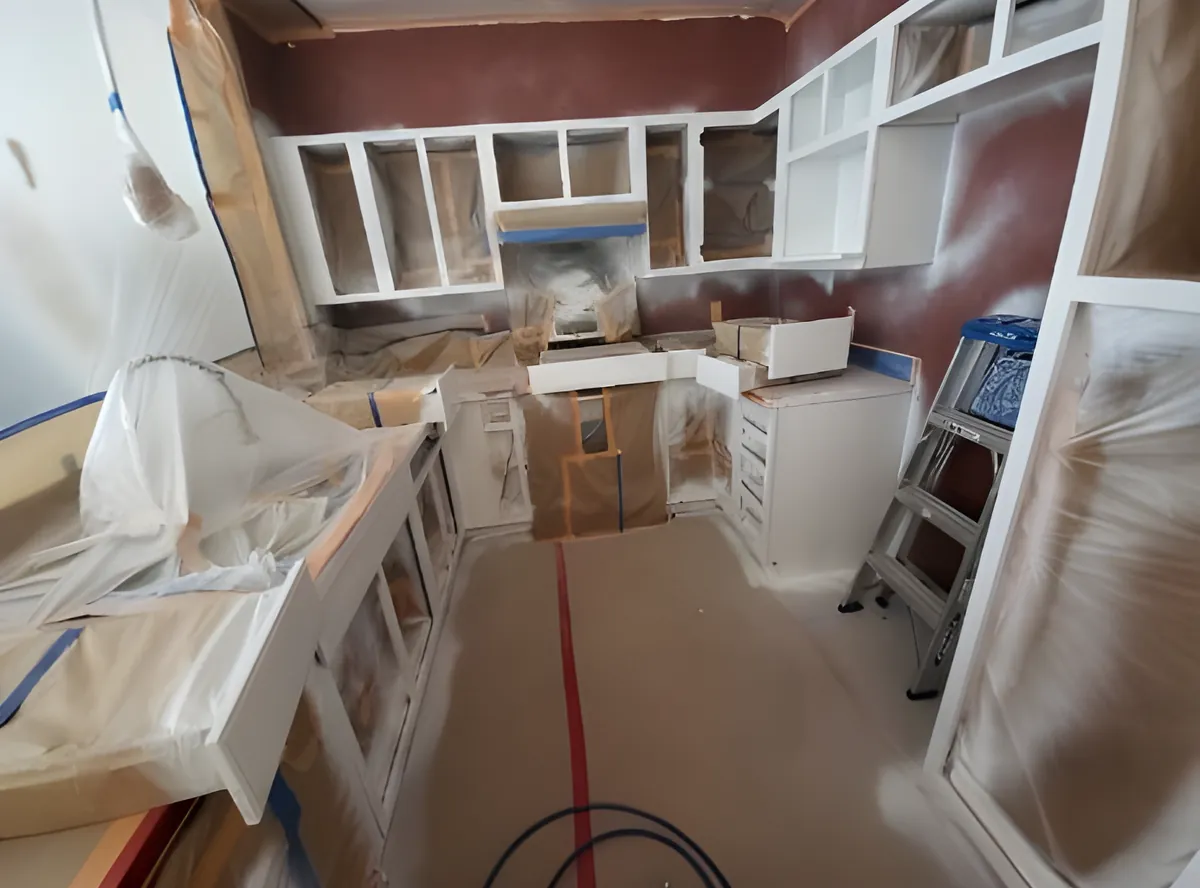 Cabinet boxes being painted white inside a kitchen sealed with plastic