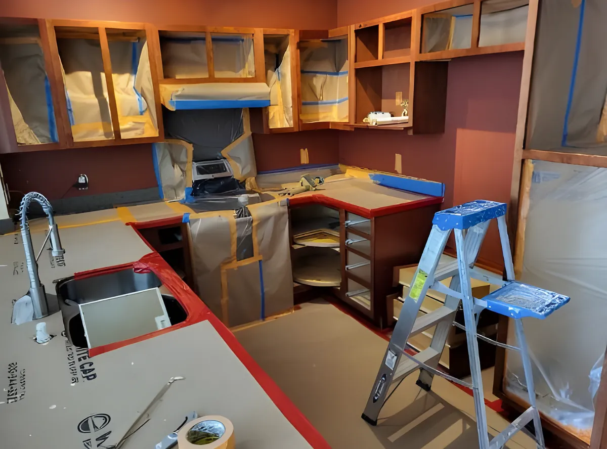 A kitchen masked off in tape and paper with the cabinet doors removed