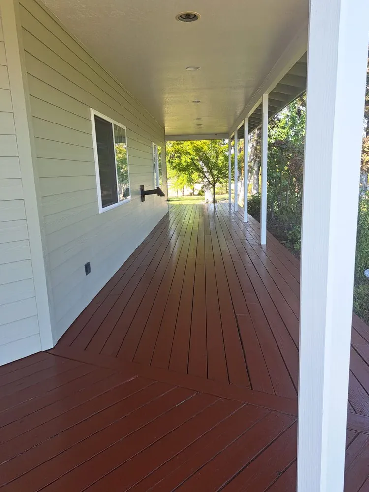 A covered porch floor stained red-brown beside white siding