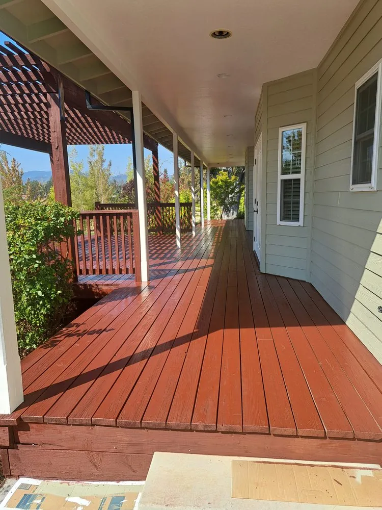 A long wraparound porch deck freshly stained red-brown along a sage green house