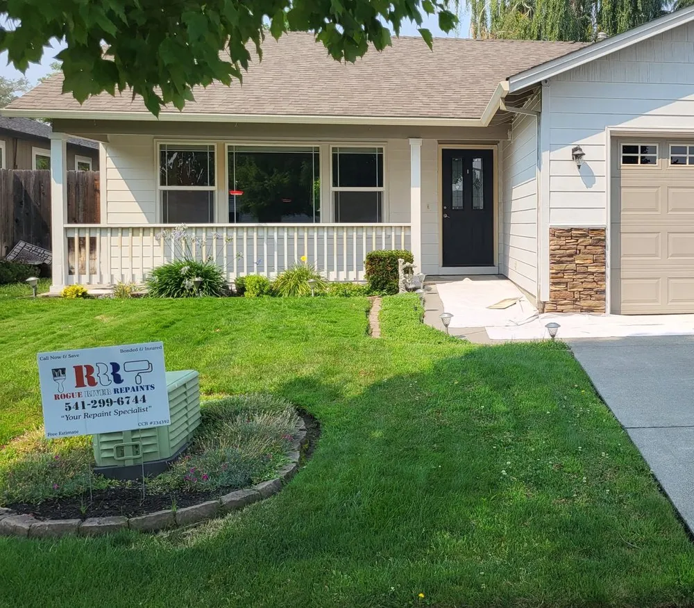 A cream house with a white porch rail and a Rogue River Repaints yard sign
